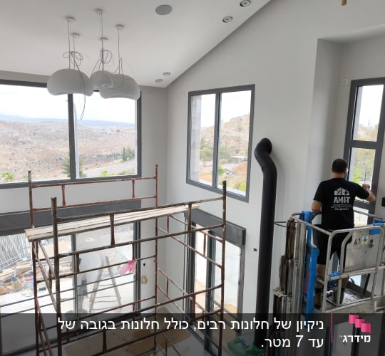 אדם מנקה חלונות בעזרת מנוף בתוך בית